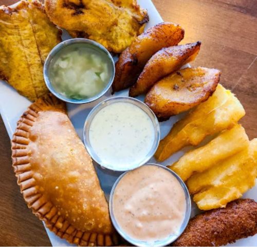 A platter of assorted fried foods including empanadas, plantains, and dipping sauces.