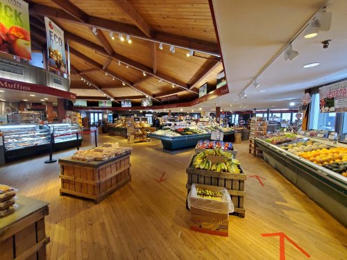 A spacious market interior with wooden beams, showcasing fresh produce, baked goods, and various food displays.