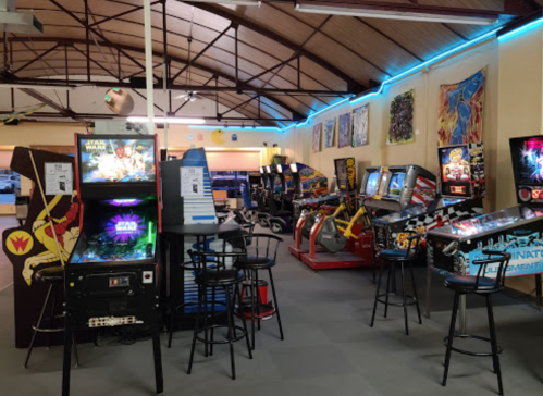 A vibrant arcade filled with various classic arcade machines and pinball games, featuring colorful decor and seating.