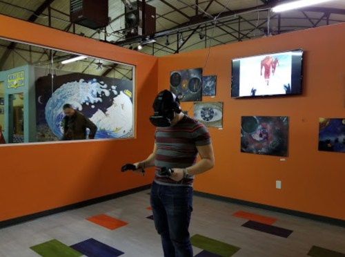 A person wearing a VR headset stands in an art gallery with colorful walls and space-themed artwork.