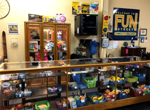 A colorful arcade counter with toys and games, featuring a display case and a "Welcome to Fun Street" sign.