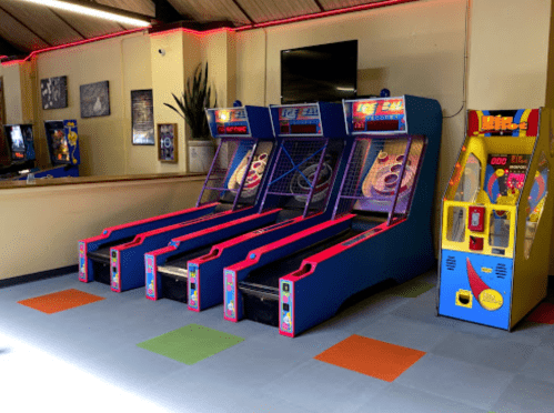 Three ice hockey arcade games and a claw machine in a brightly lit game room. Colorful floor tiles are visible.