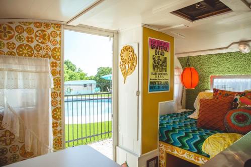 Interior of a colorful camper with a view of a pool outside, featuring vibrant decor and a Grateful Dead poster.