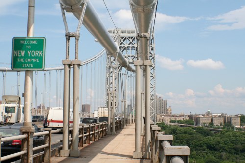 View of the George Washington Bridge with a "Welcome to New York" sign and city skyline in the background.