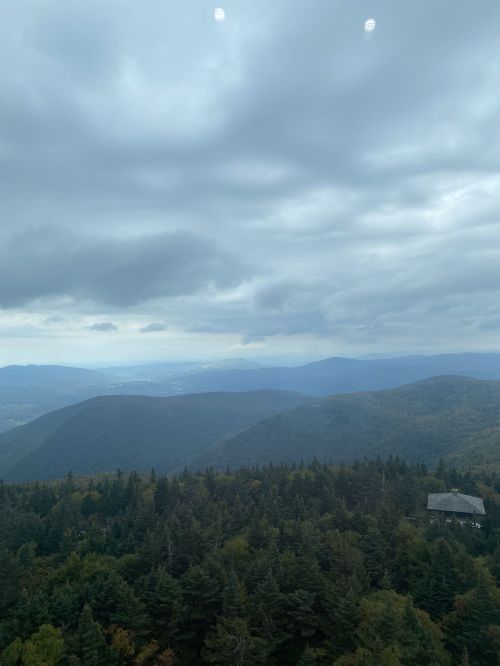 A panoramic view of rolling mountains and dense forests under a cloudy sky.