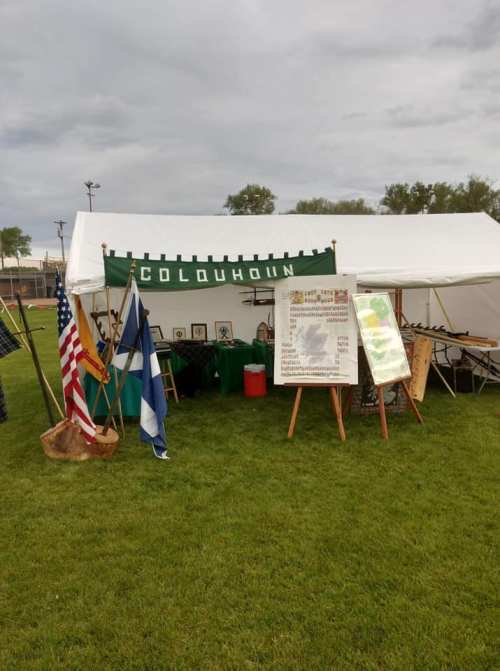 A tent displaying flags and informational boards on a grassy field, with a cloudy sky in the background.