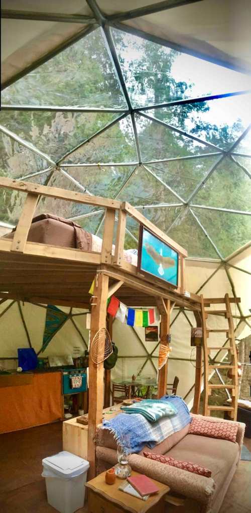 Interior of a geodesic dome with a loft, wooden furniture, colorful decor, and a cozy living area.