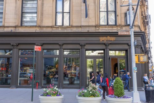 Exterior of a Harry Potter-themed store on a city street, featuring large windows and colorful flower planters.