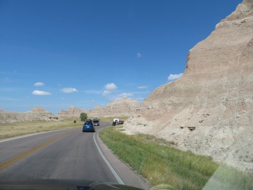 A scenic road winds through rocky terrain under a clear blue sky, with vehicles traveling along the route.