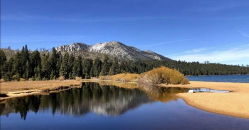 A serene lake surrounded by mountains and trees, reflecting the clear blue sky and autumn foliage.