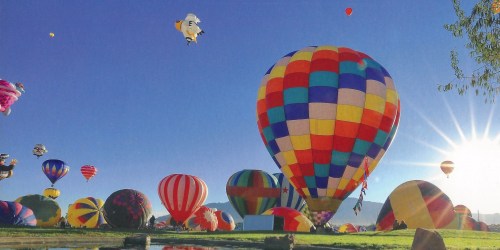 A vibrant scene of colorful hot air balloons in a clear blue sky, with the sun shining in the background.