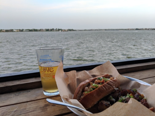 A scenic view of a lake with two hot dogs and a glass of beer on a wooden table.