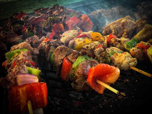 Grilled skewers of meat and colorful vegetables sizzling on a barbecue, surrounded by smoke.
