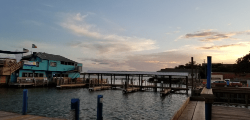 A waterfront scene at sunset featuring docks, a colorful building, and a calm waterway with clouds in the sky.