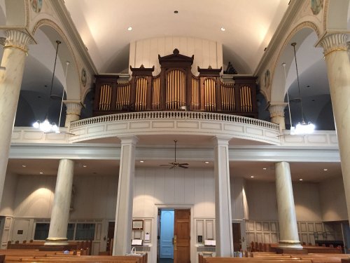 Interior of a church featuring a large pipe organ above a spacious seating area with columns and soft lighting.