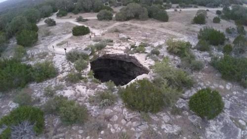 Aerial view of a large sinkhole surrounded by rocky terrain and sparse vegetation.