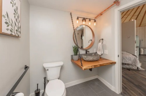 Modern bathroom featuring a round mirror, wooden sink, and stylish lighting, with a toilet and neutral decor.