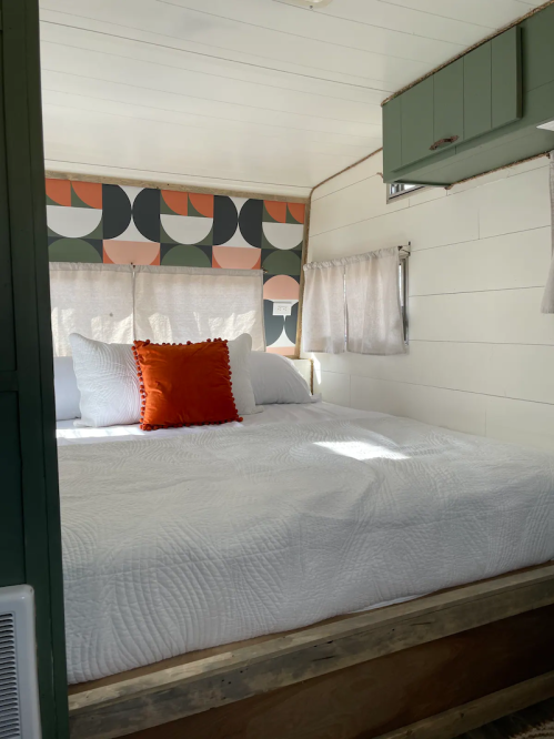 Cozy bedroom with a large bed, colorful patterned wall, and natural light streaming through the windows.
