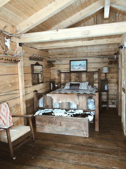 Cozy wooden cabin bedroom with a bed, rustic decor, and a chair, featuring a warm, inviting atmosphere.