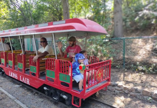 A small train with passengers, including a child in a blue hat, riding through a wooded area.