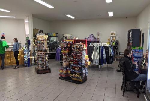 A small shop interior with shelves of merchandise, snacks, and clothing, and customers browsing and seated.