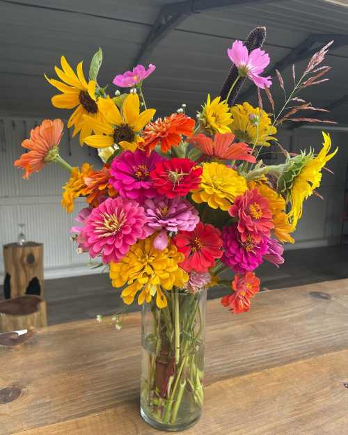 A vibrant bouquet of mixed flowers in a clear vase, featuring bright colors like pink, orange, yellow, and purple.