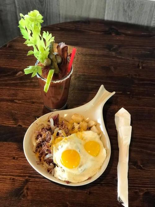 A plate with two sunny-side-up eggs on a bed of cabbage, alongside a Bloody Mary garnished with celery and bacon.