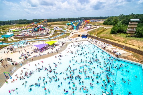 Aerial view of a busy water park with pools, water slides, and crowds of people enjoying the sunny day.