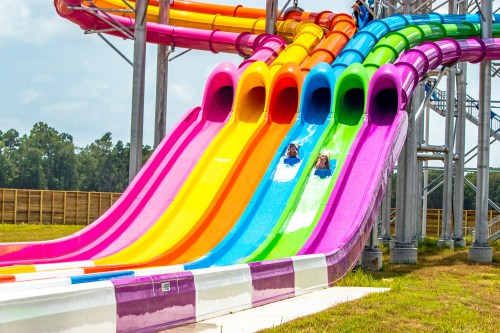 Two people slide down colorful water slides at a water park on a sunny day.