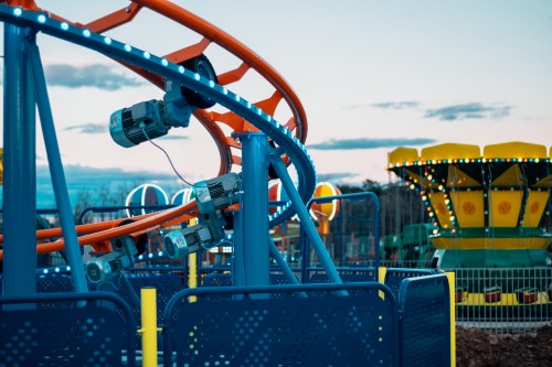 A colorful amusement park scene featuring a roller coaster track and a spinning ride in the background at dusk.