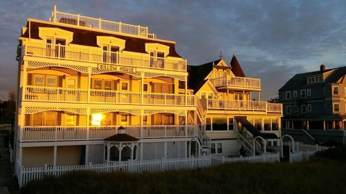 Sunset reflecting on the Billow House, a charming beachside building with multiple balconies and a white picket fence.