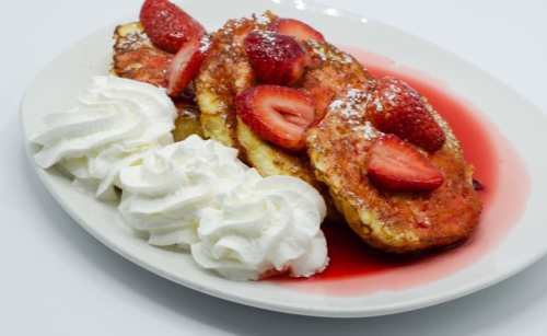 A plate of French toast topped with strawberries and whipped cream, drizzled with strawberry sauce.