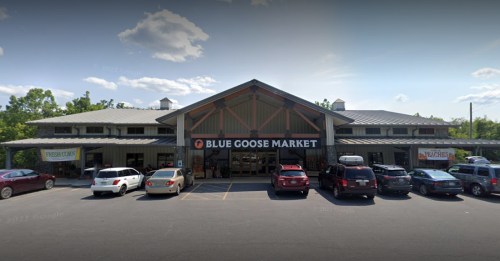 Exterior view of Blue Goose Market with a large sign, surrounded by parked cars and trees under a clear sky.