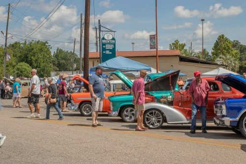 A car show featuring classic cars with people admiring them on a sunny day in a small town.