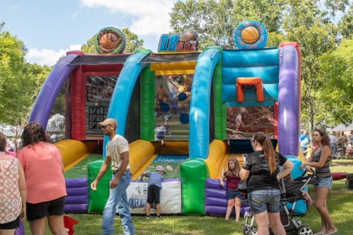 A colorful inflatable bounce house with basketball and sports themes, surrounded by people enjoying a fair.