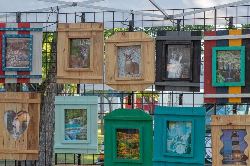 A display of framed photographs in various colors and shapes, hanging on a grid at an outdoor market.