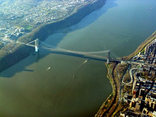 Aerial view of a bridge spanning a river, surrounded by greenery and urban areas.