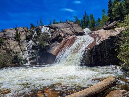 A scenic waterfall cascading over rocky cliffs, surrounded by lush greenery and a clear blue sky.