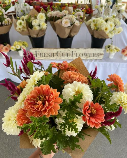 A hand holding a bouquet of vibrant flowers, with a backdrop of more flower arrangements on display.