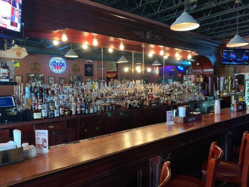 A well-stocked bar with numerous bottles of liquor displayed on shelves, illuminated by warm lights.