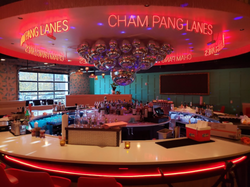 A vibrant bar area with a modern design, featuring colorful lighting and a large chandelier of disco balls.