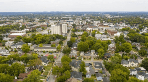 Aerial view of a cityscape featuring residential areas, trees, and a skyline with low-rise buildings.