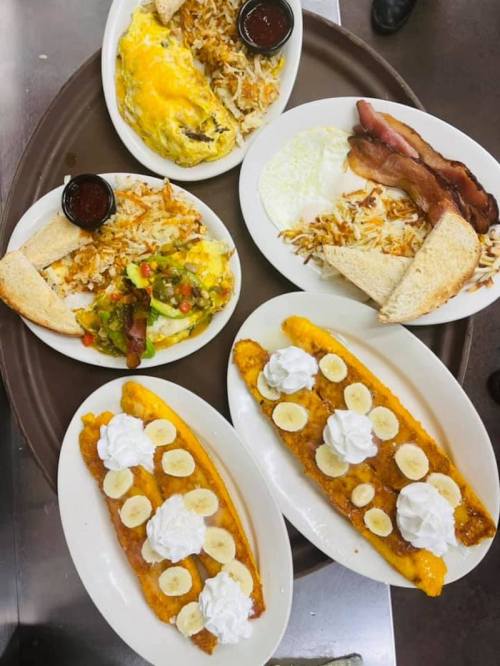 A platter of breakfast dishes including omelets, bacon, eggs, toast, and banana pancakes with whipped cream.