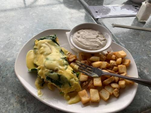 A plate of spinach omelette topped with cheese, served with a side of creamy sauce and golden-brown diced potatoes.
