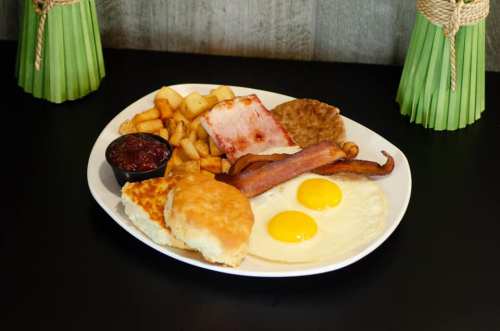A breakfast plate featuring eggs, bacon, sausage, hash browns, biscuits, and a side of jam.