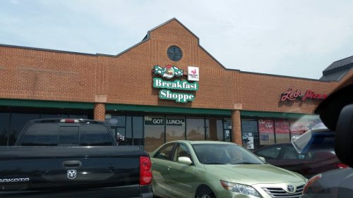 Exterior of a restaurant called "Breakfast Shoppe," with a sign and parked cars in front.
