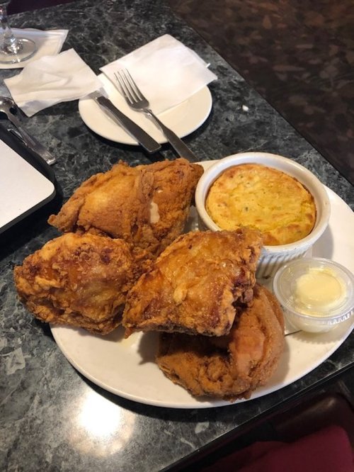 A plate with four pieces of fried chicken, a small dish of cornbread, and a cup of butter on a marble table.