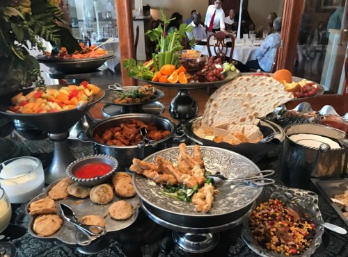 A buffet table filled with various dishes, including fruits, fried chicken, bread, and desserts, in an elegant setting.