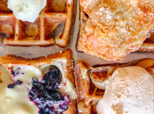 A close-up of four waffles topped with various ingredients, including ice cream, fruit, and whipped cream.