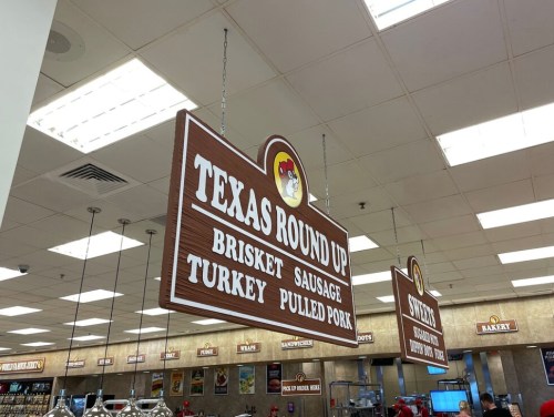 Signage for "Texas Round Up" featuring brisket, sausage, turkey, and pulled pork in a food court setting.
